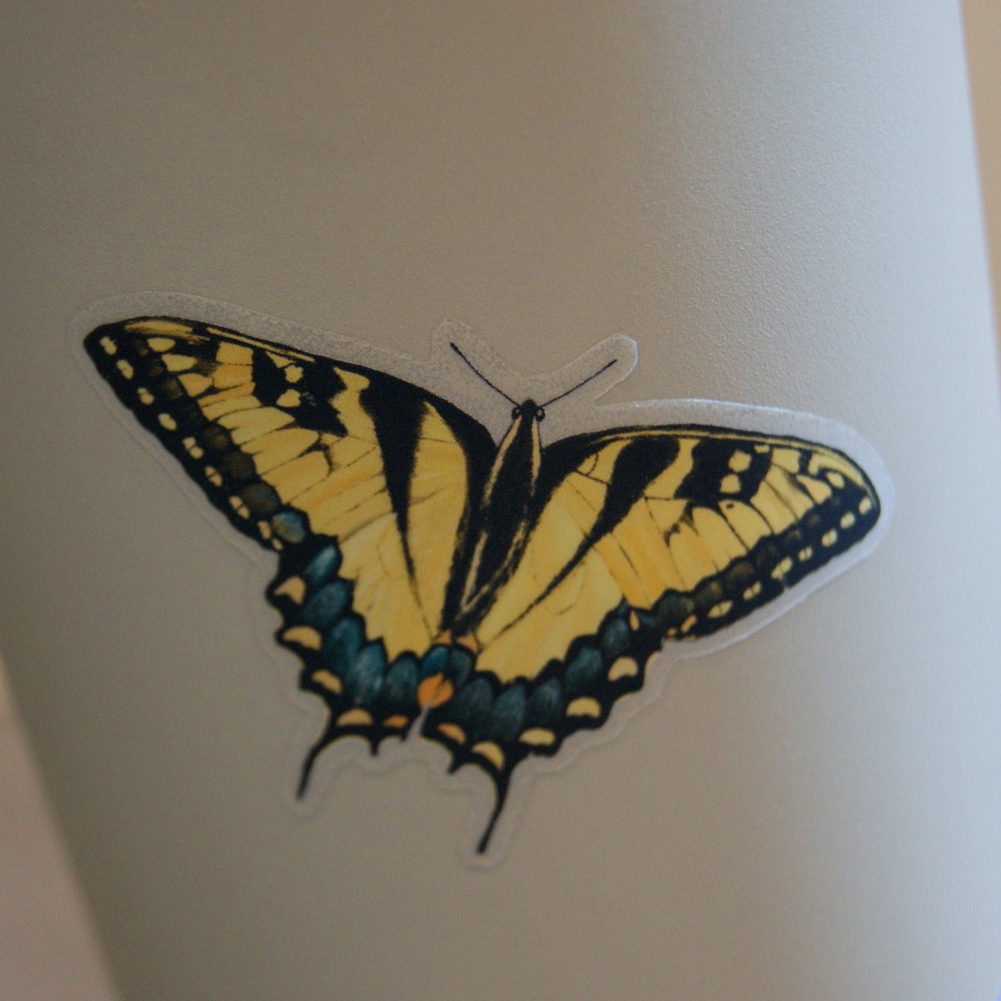 Die-cut clear vinyl sticker that measures 2.4" long by 1.6" high featuring hand-drawn yellow swallowtail butterfly. Displayed on a taupe tumbler to showcase the clear vinyl background.